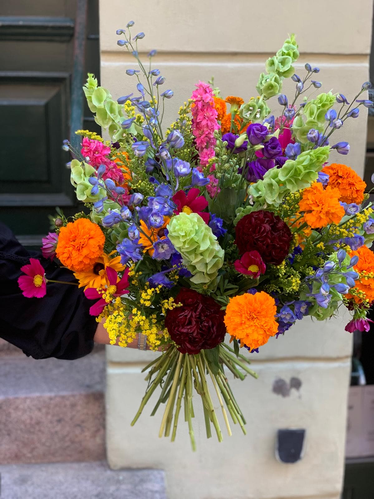 Håndbundet buket med sommerblomster holdt for en dør