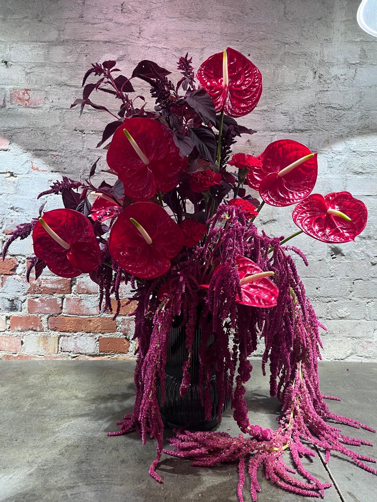 Høj dekoration med røde anthurier og hængende amaranthus i en ribbet sort vase